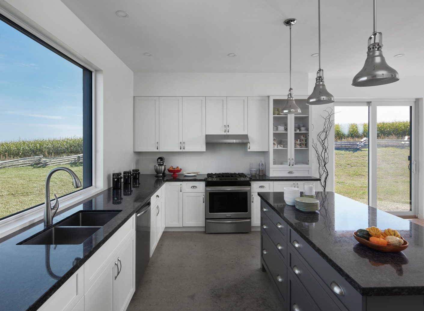 Interior of a kitchen with white cabintery and dark stone countertops with window and sliding patio door facing a field.
