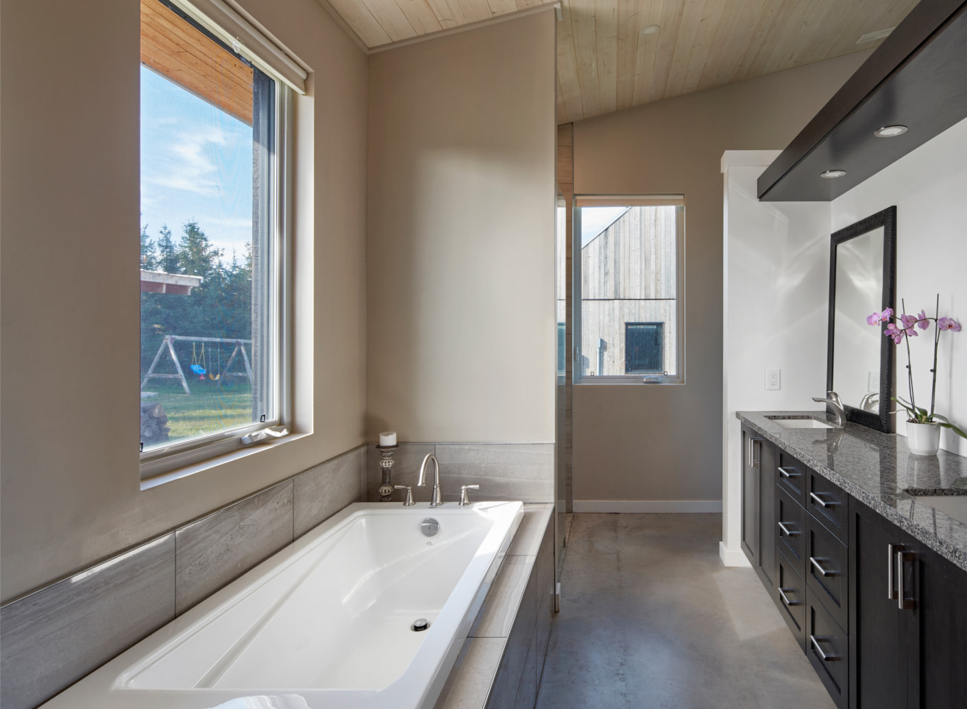 Interior of a bathroom with a bathtub, light brown walls and dark stone countertop with a sink.